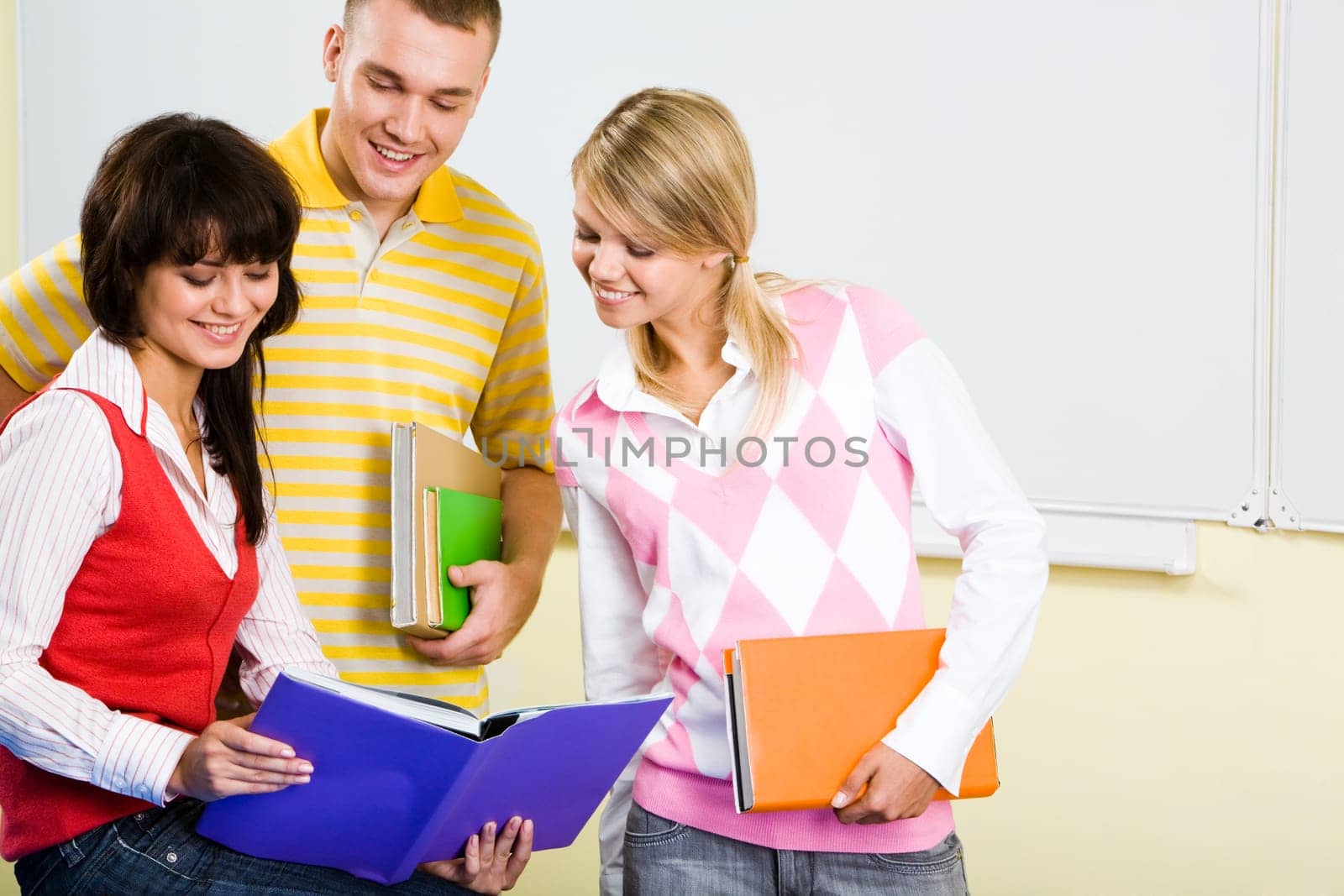 Image of three teens looking into textbook with smiles while preparing for the lesson