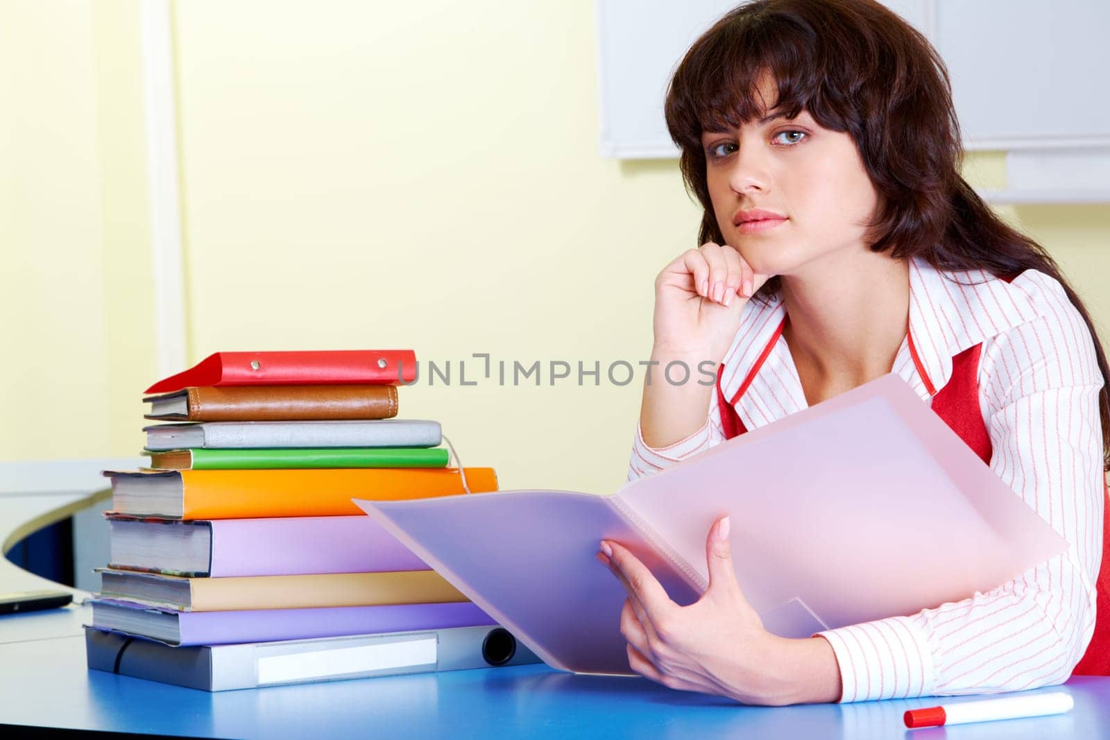 Photo of pensive teacher sitting at the desk and looking at camera