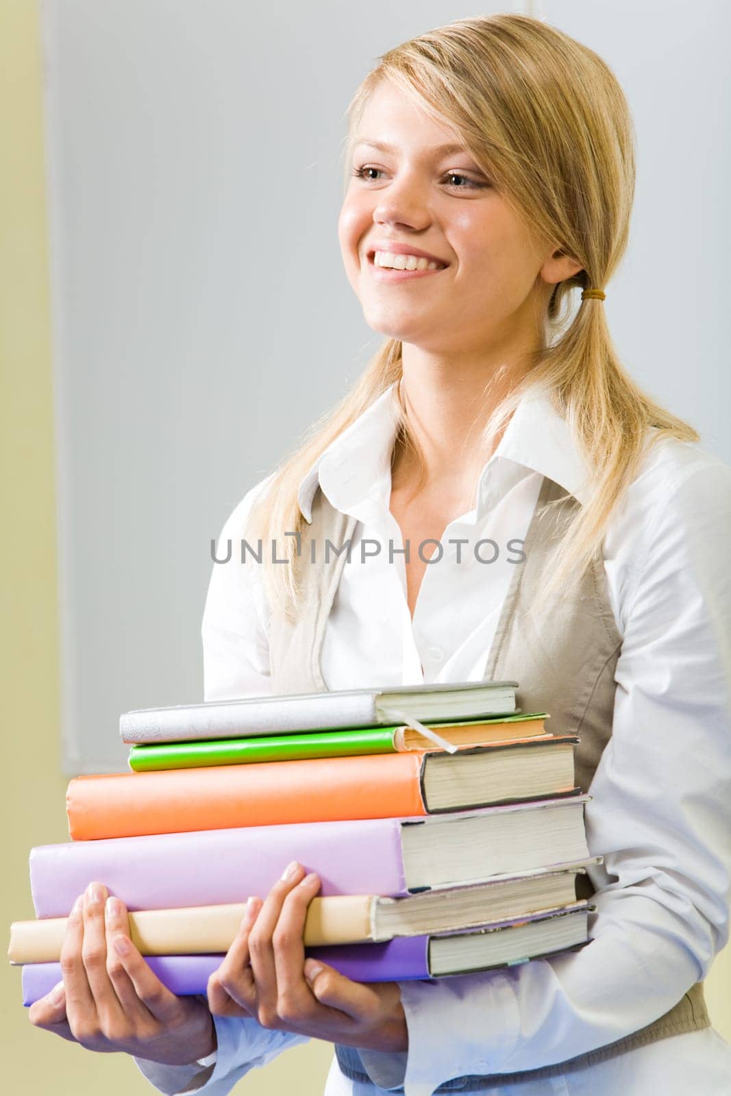 Portrait of cheerful student with pile of books in hands
