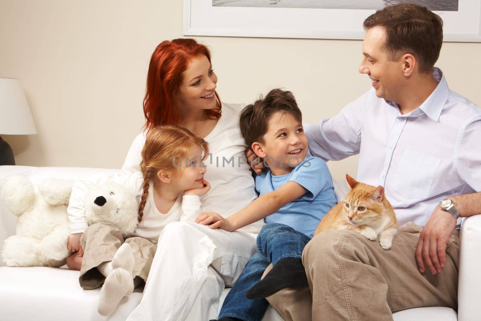 Curious children and woman looking attentively at handsome man while relaxing on sofa