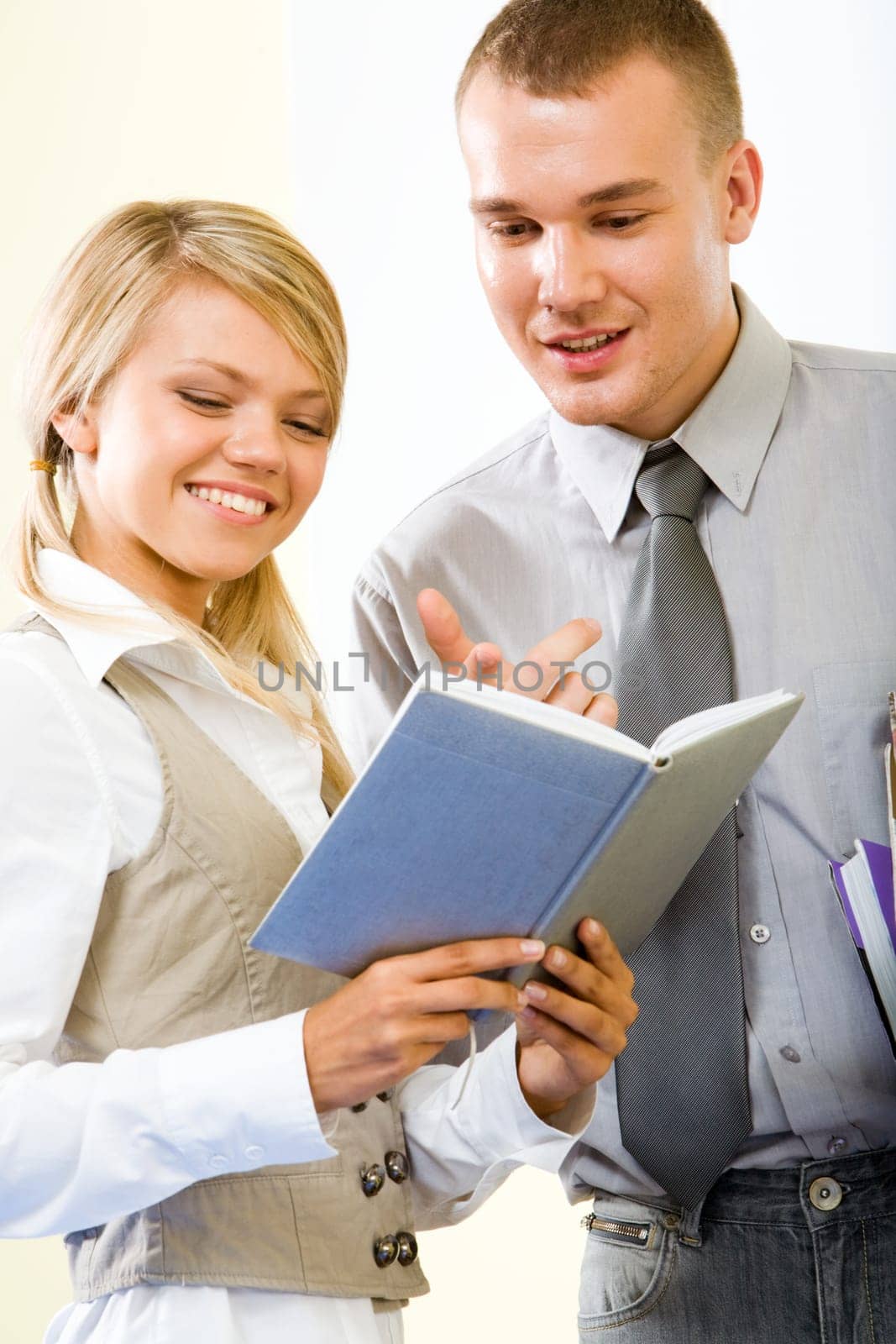 Portrait of smart guy pointing at notebook and explaining something to smiling girl