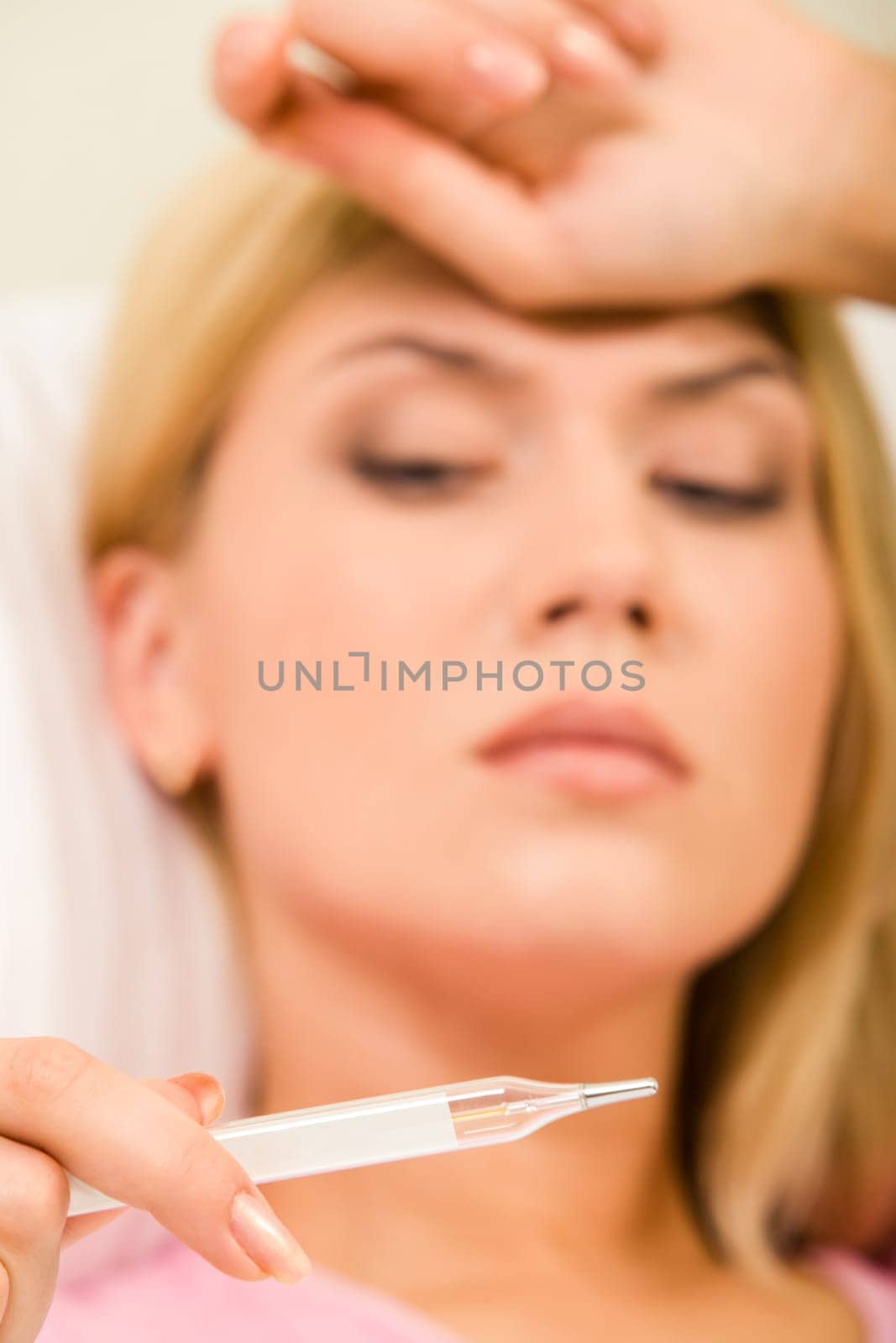 Close-up of females hand holding thermometer with woman looking at it on background