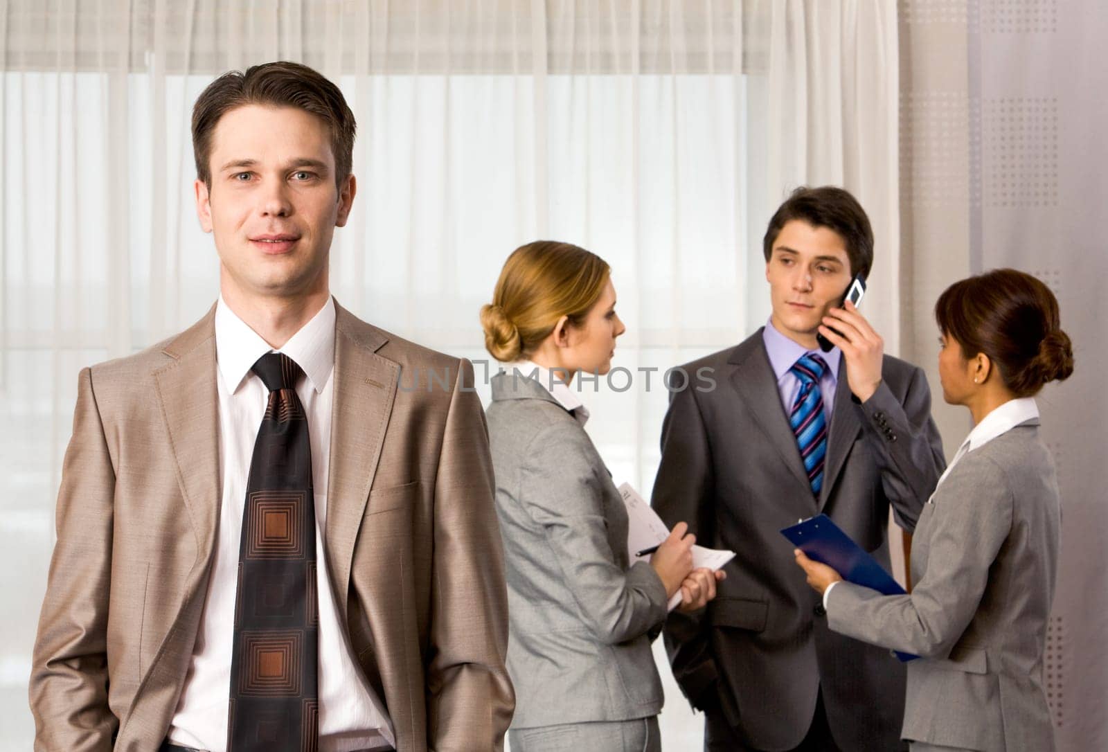 Portrait of handsome employer smiling at camera with consulting staff on background