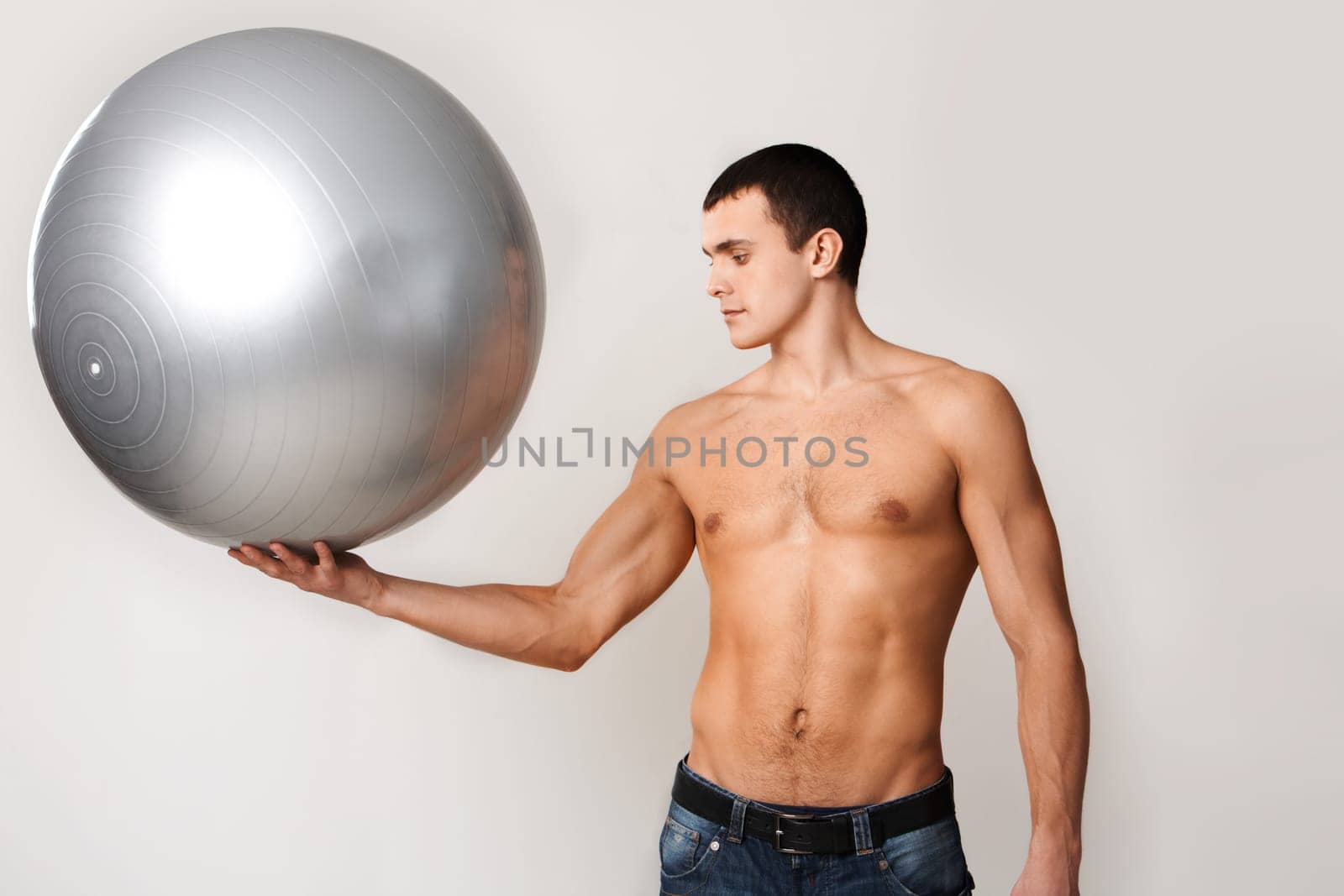 Portrait of shirtless man in jeans holding big ball on hand
