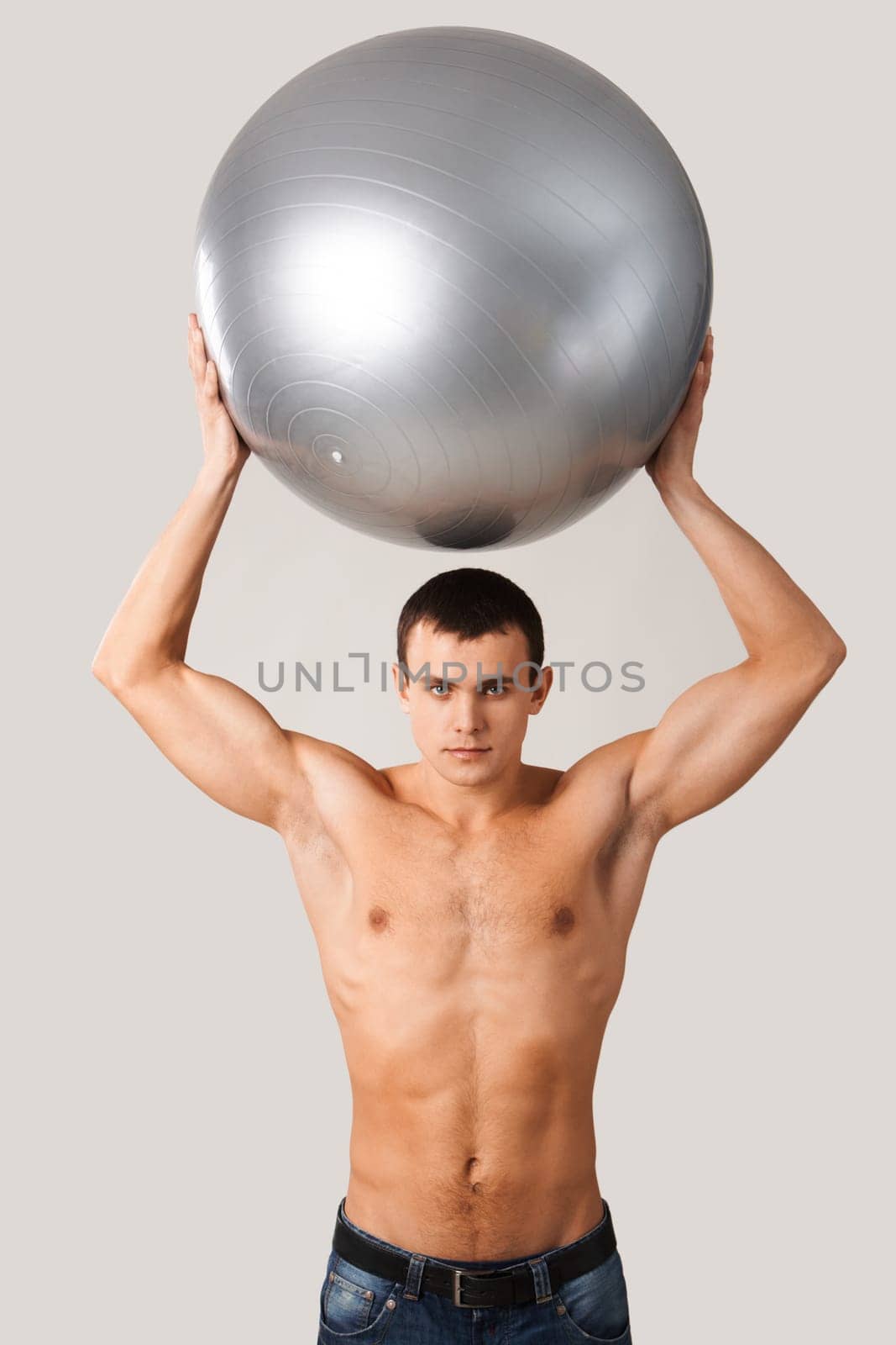 Portrait of shirtless man in jeans holding big ball over his head