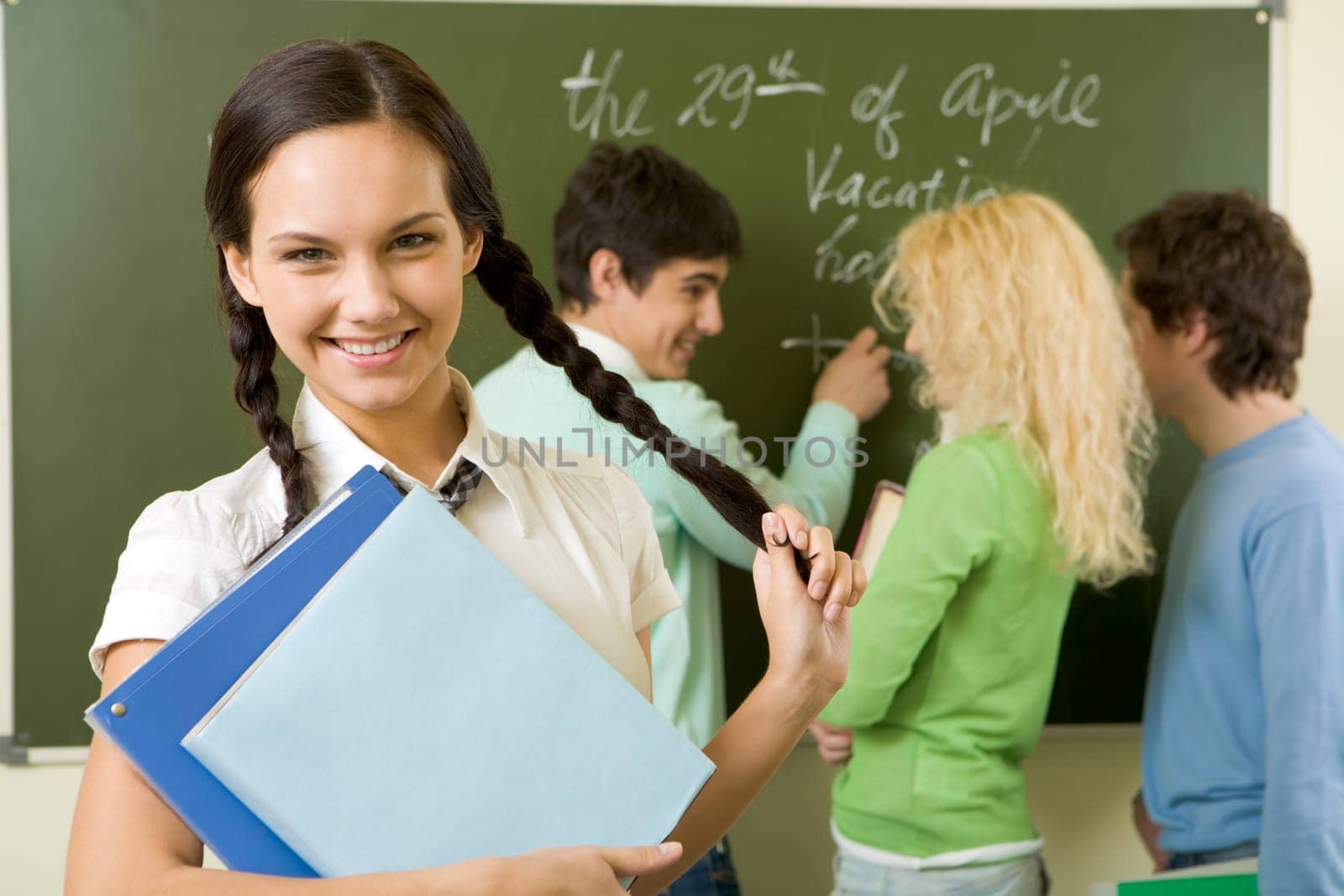 Portrait of cute girl holding textbook in hands on background of communicating students