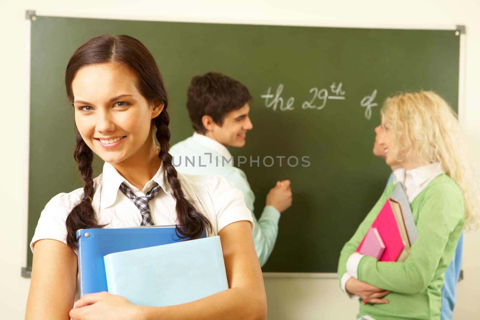 Portrait of cute girl holding textbooks in hands on background of communicating groupmates