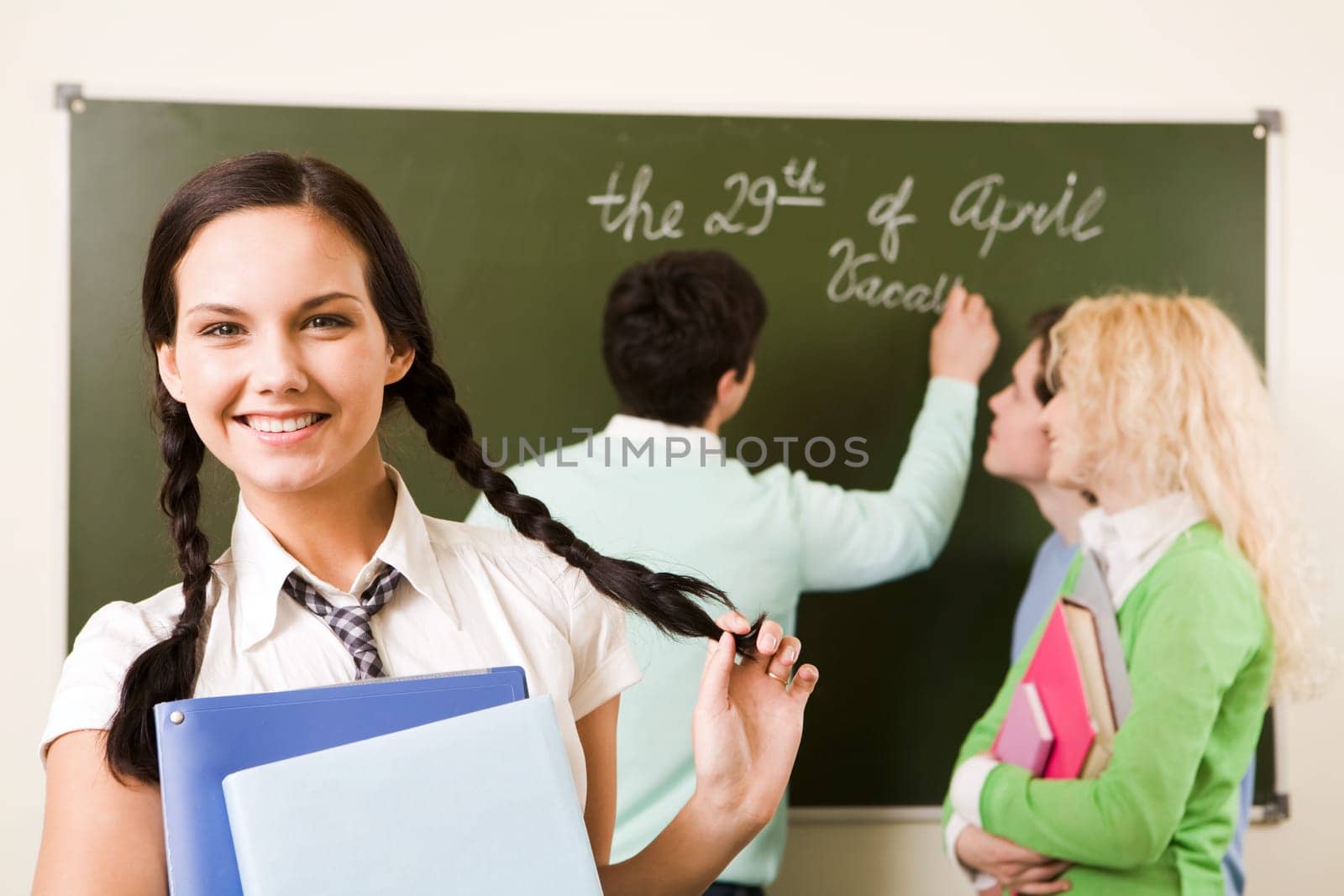 Portrait of cute girl holding textbook in hands on background of communicating students