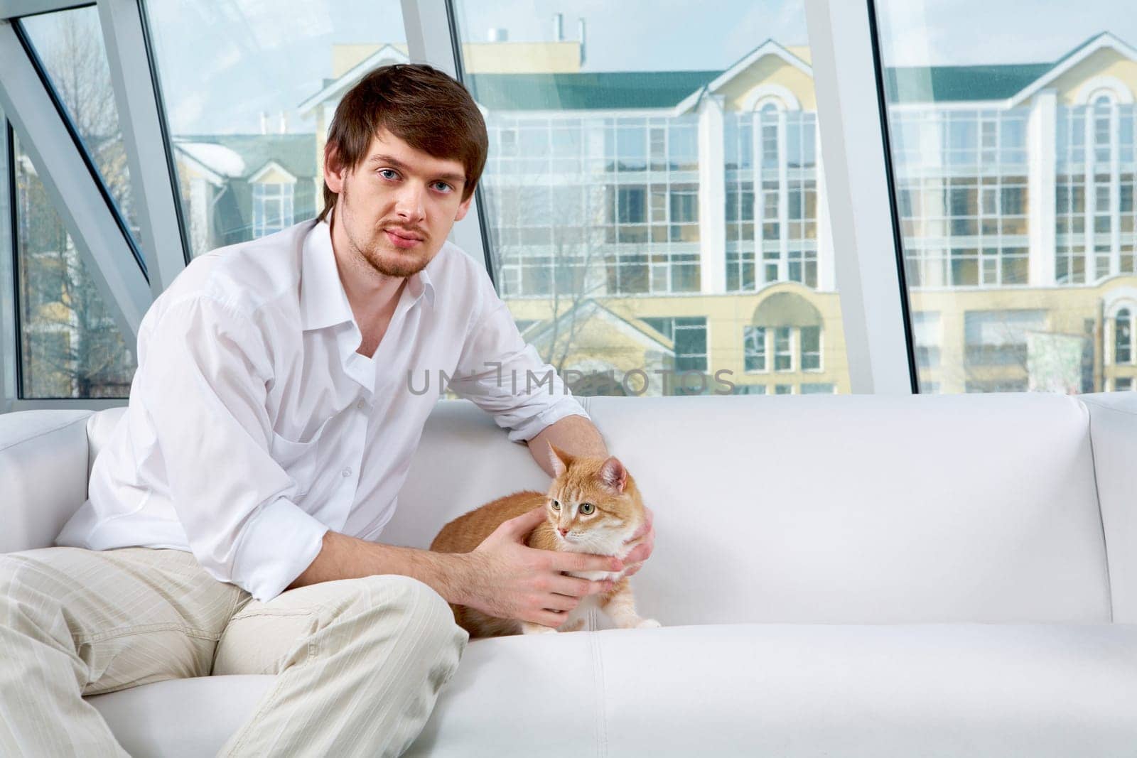A man sitting on sofa with a cat and looking at camera
