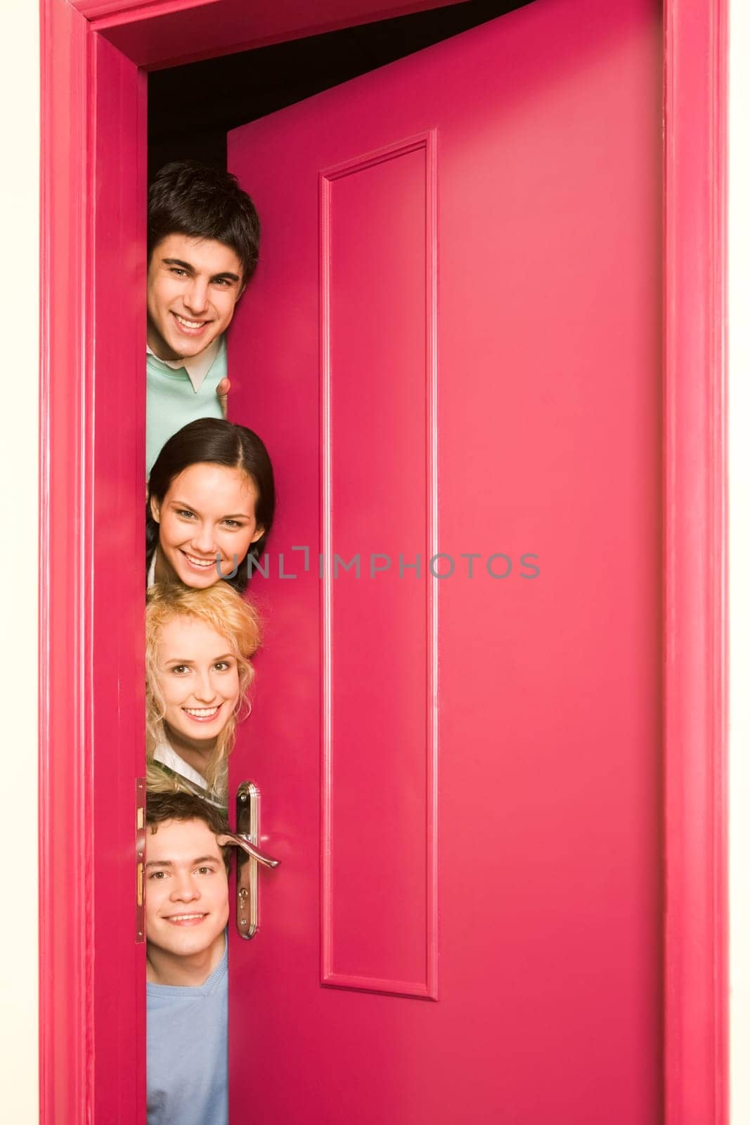 Portrait of happy students looking from behind door at camera with smiles