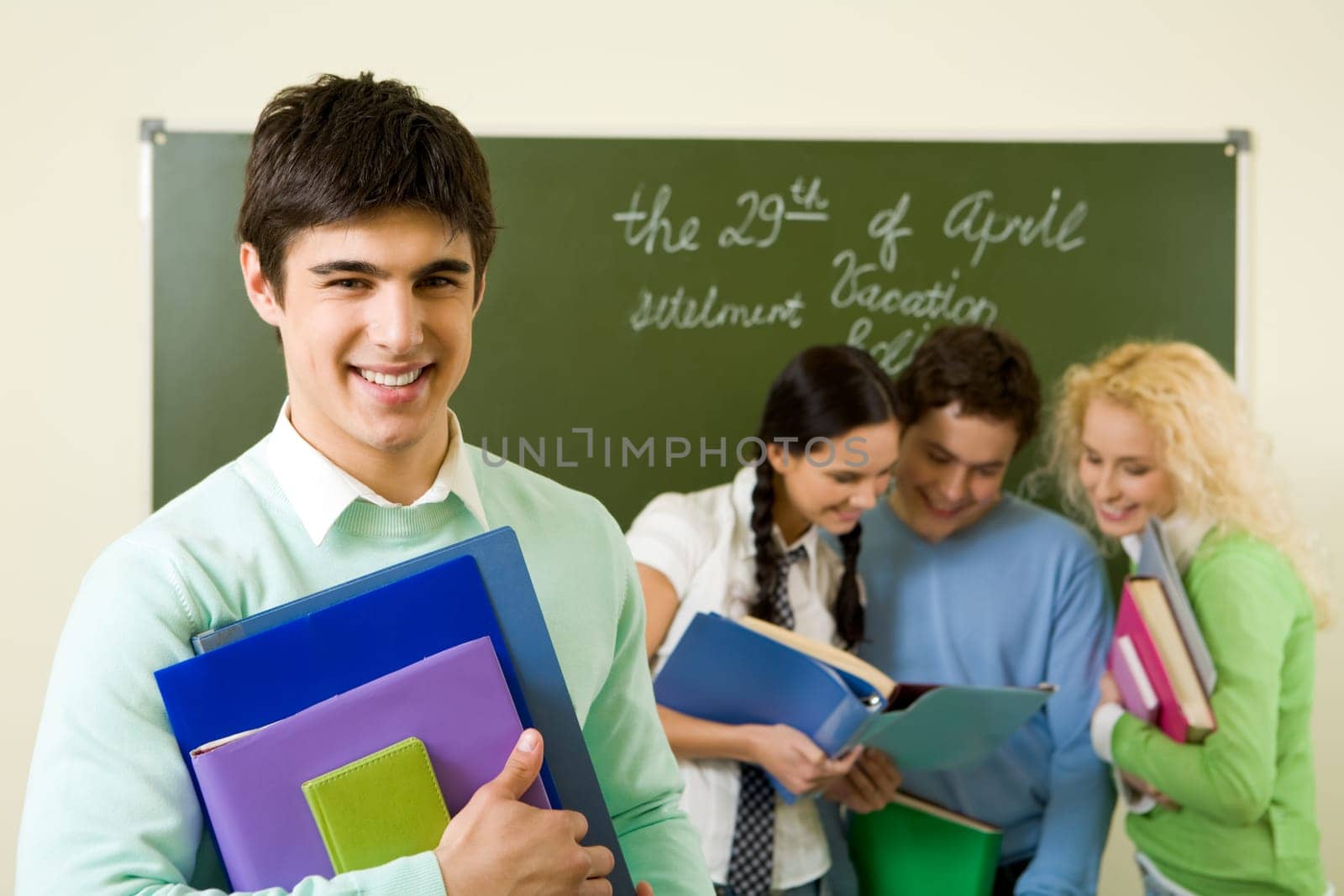 Portrait of successful student with textbooks in hands on background of reading groupmates