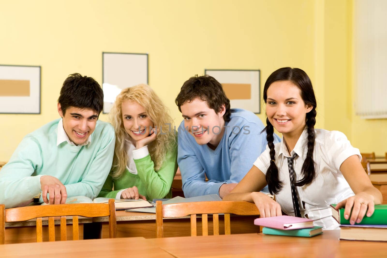 Portrait of happy students sitting at their tables and looking at camera with smiles during lesson