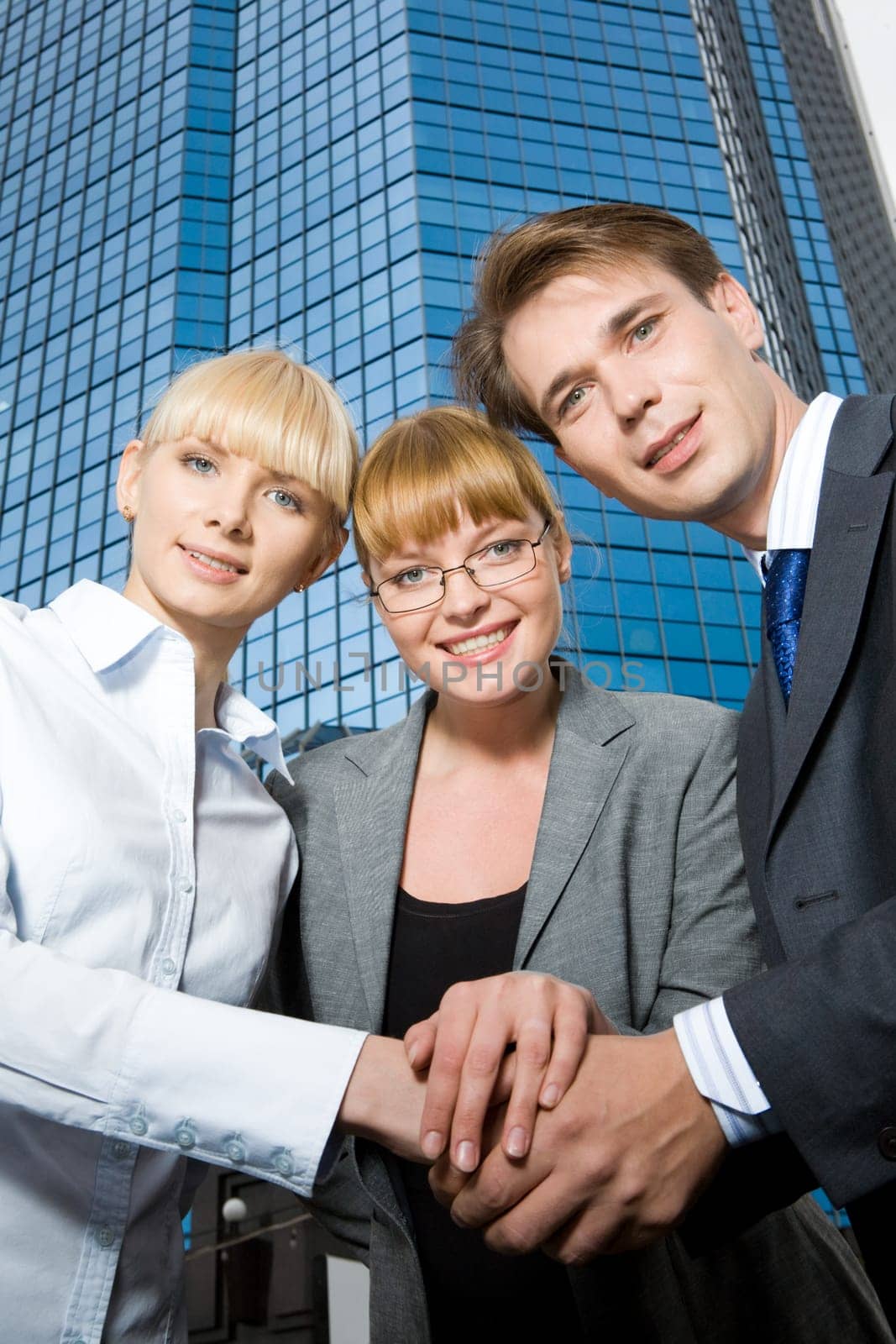 Portrait of happy business people making pile of hands and looking at camera on background of office building