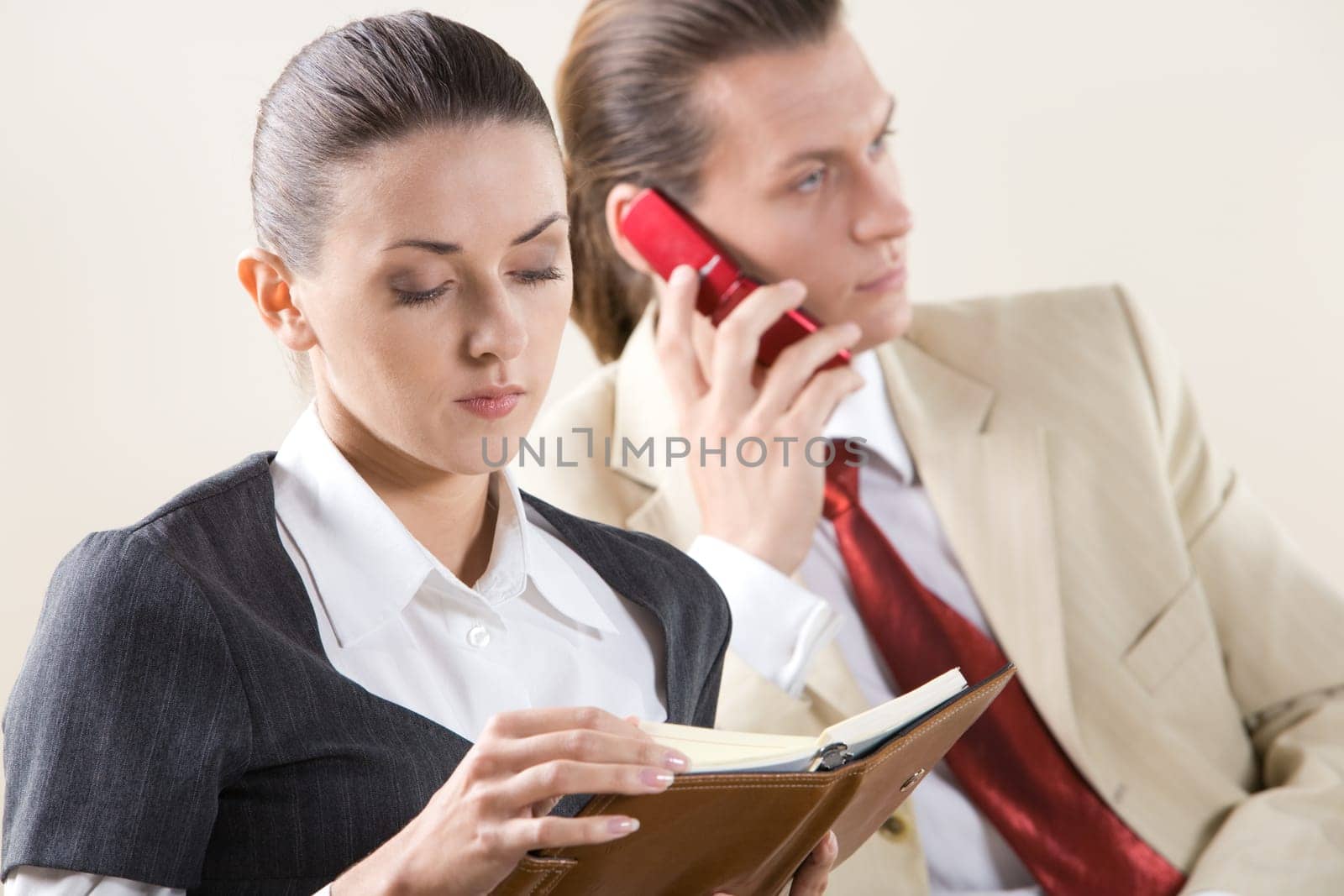 Portrait of pretty employee looking into notebook on background of man talking on the phone