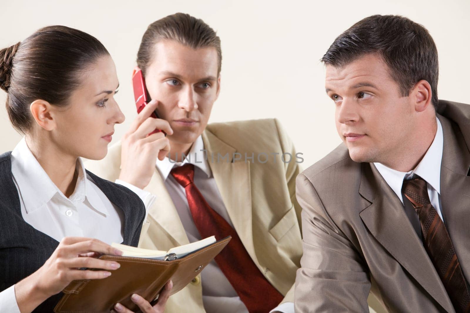 Photo of two colleagues looking at each other during meeting on background of phoning man