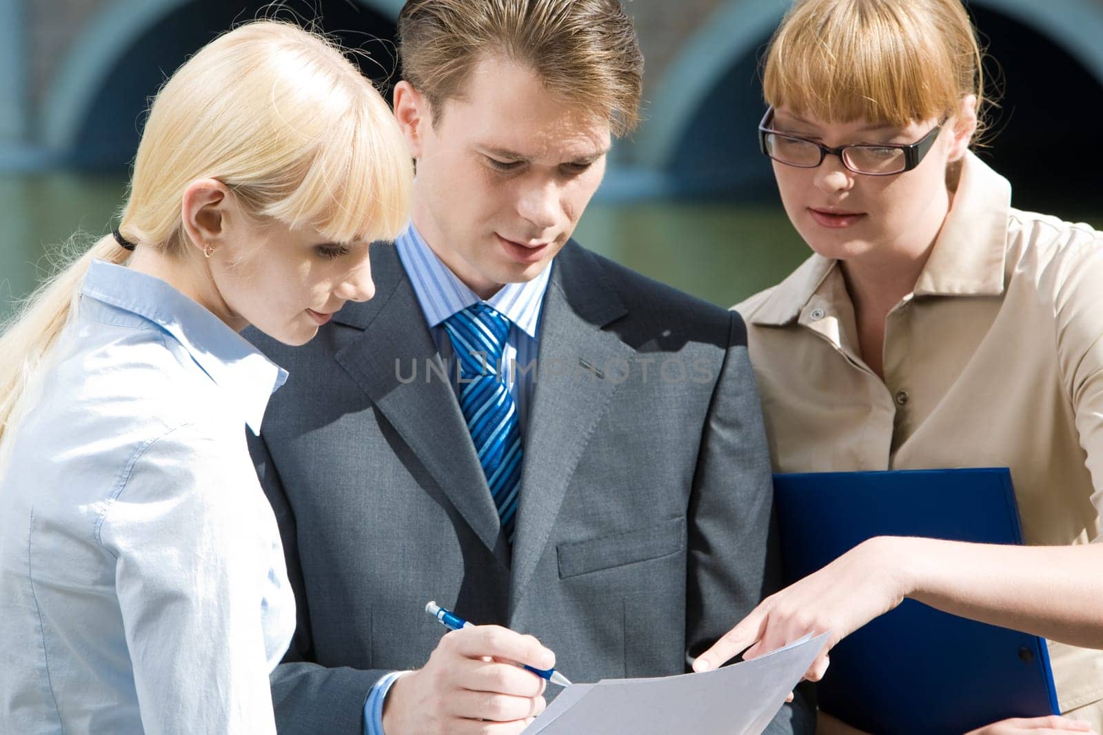 Portrait of friendly business team looking at document in mans hands and talking