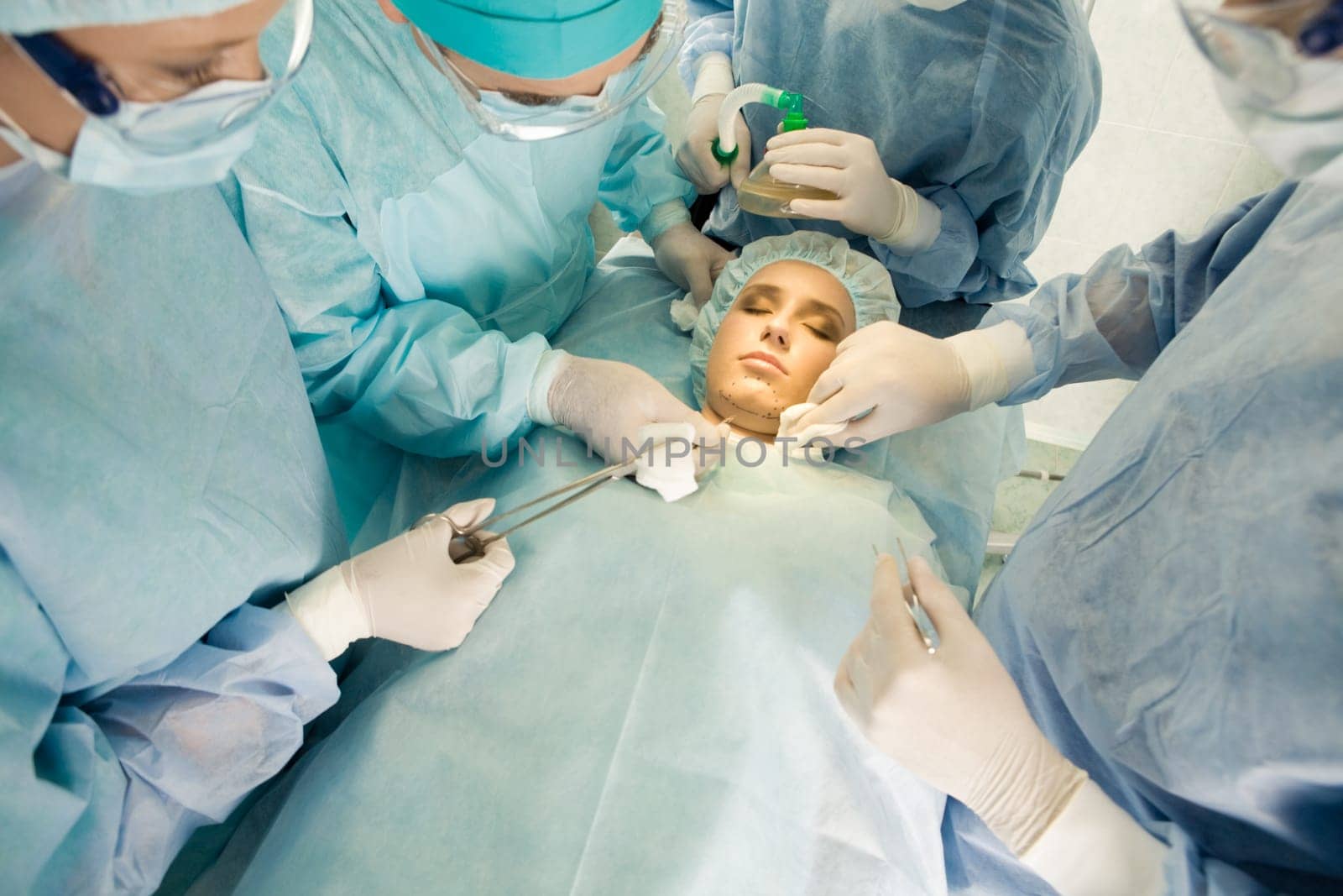 View from above of lying patient with closed eyes and doctors inclining to her