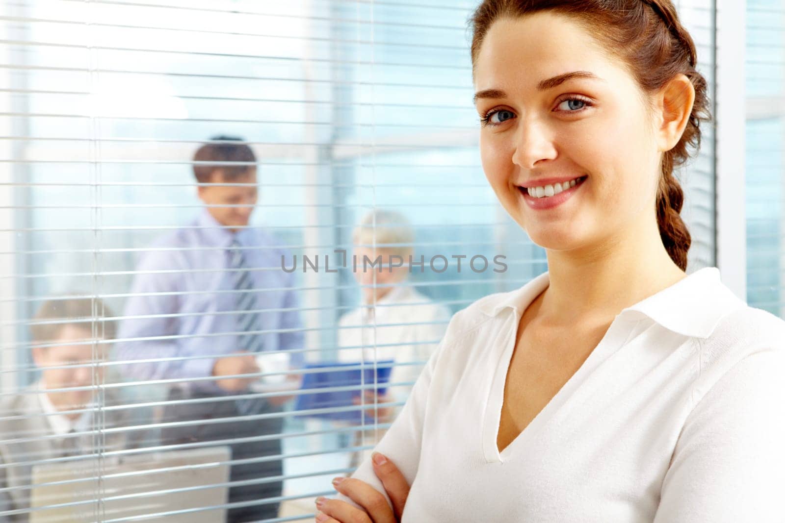 Female leader looking at camera with team of partners working in office behind