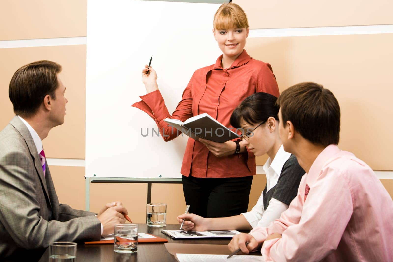 Photo of smart woman pointing at whiteboard at seminar while business partners listening to her