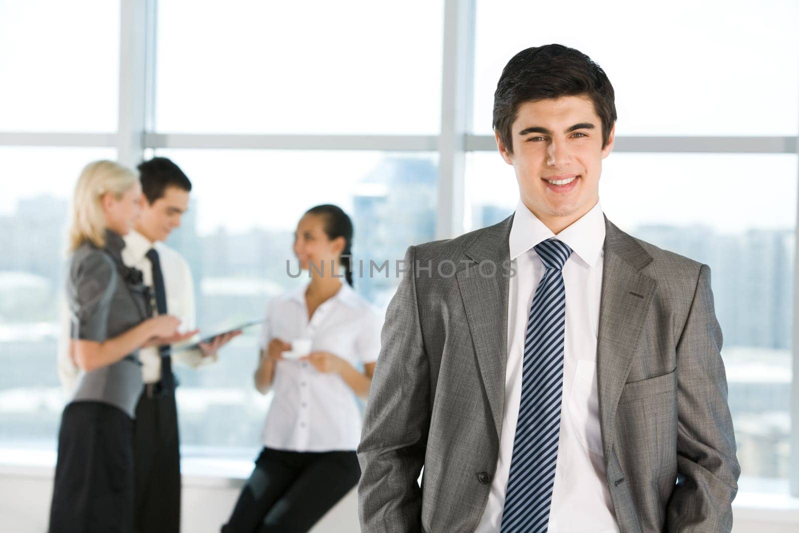 Portrait of happy businessman smiling at camera on background of interacting employees