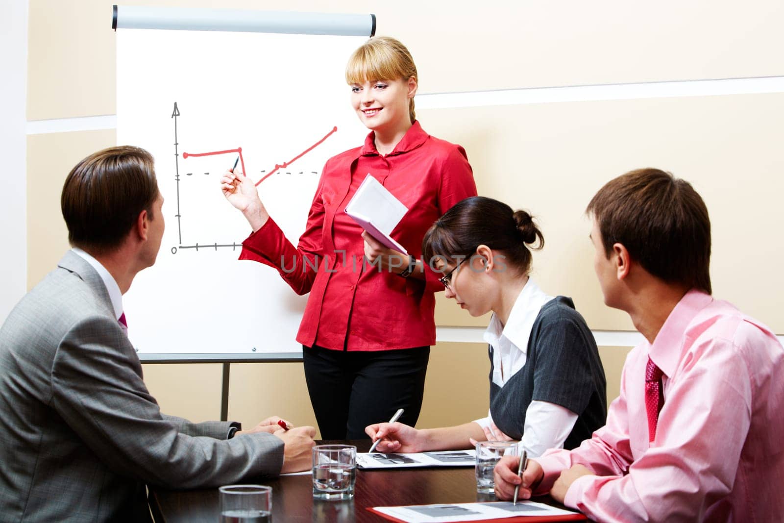 Photo of smart woman pointing at whiteboard at seminar while business partners listening to her