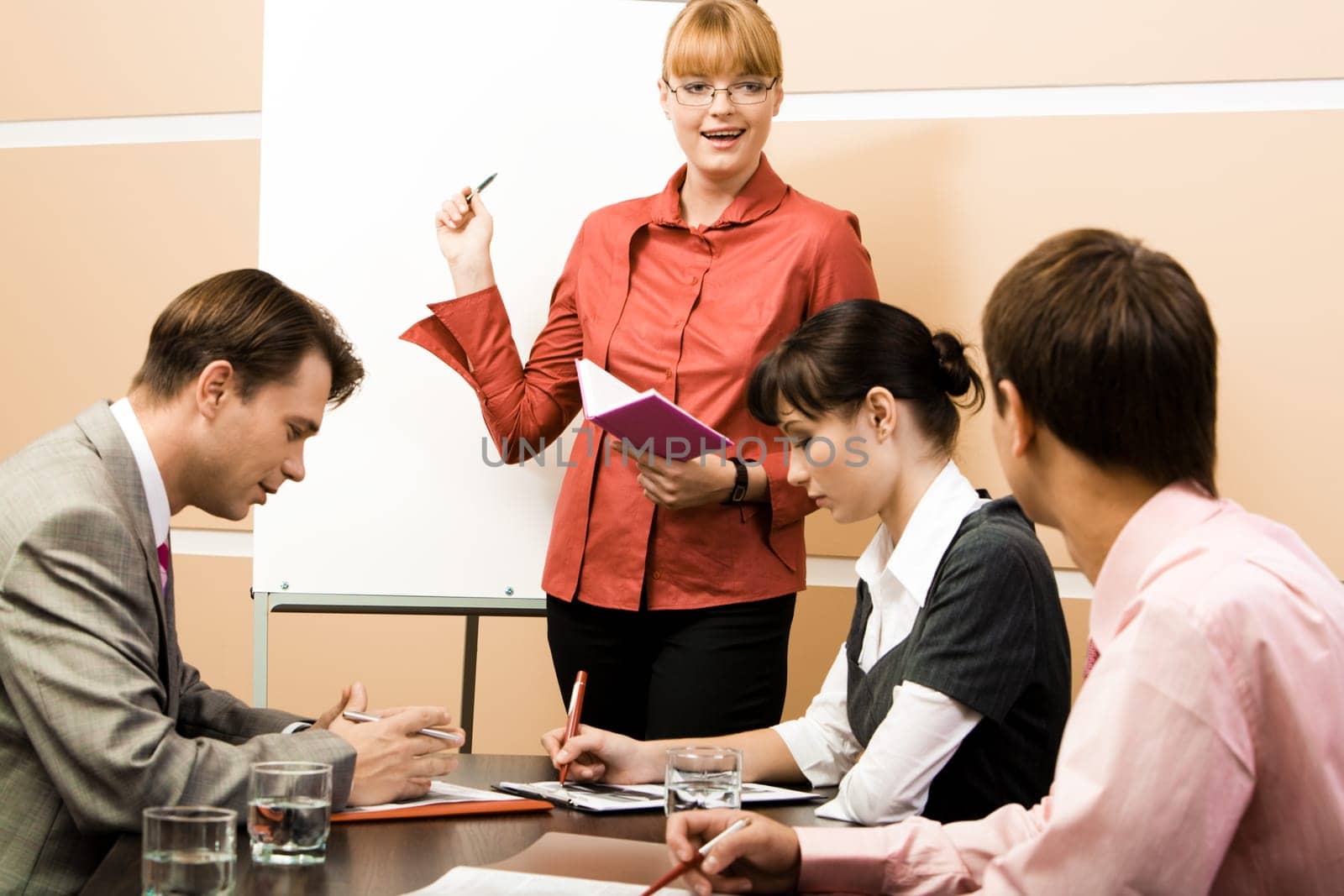 Photo of smart woman pointing at whiteboard at seminar while business partners listening to her