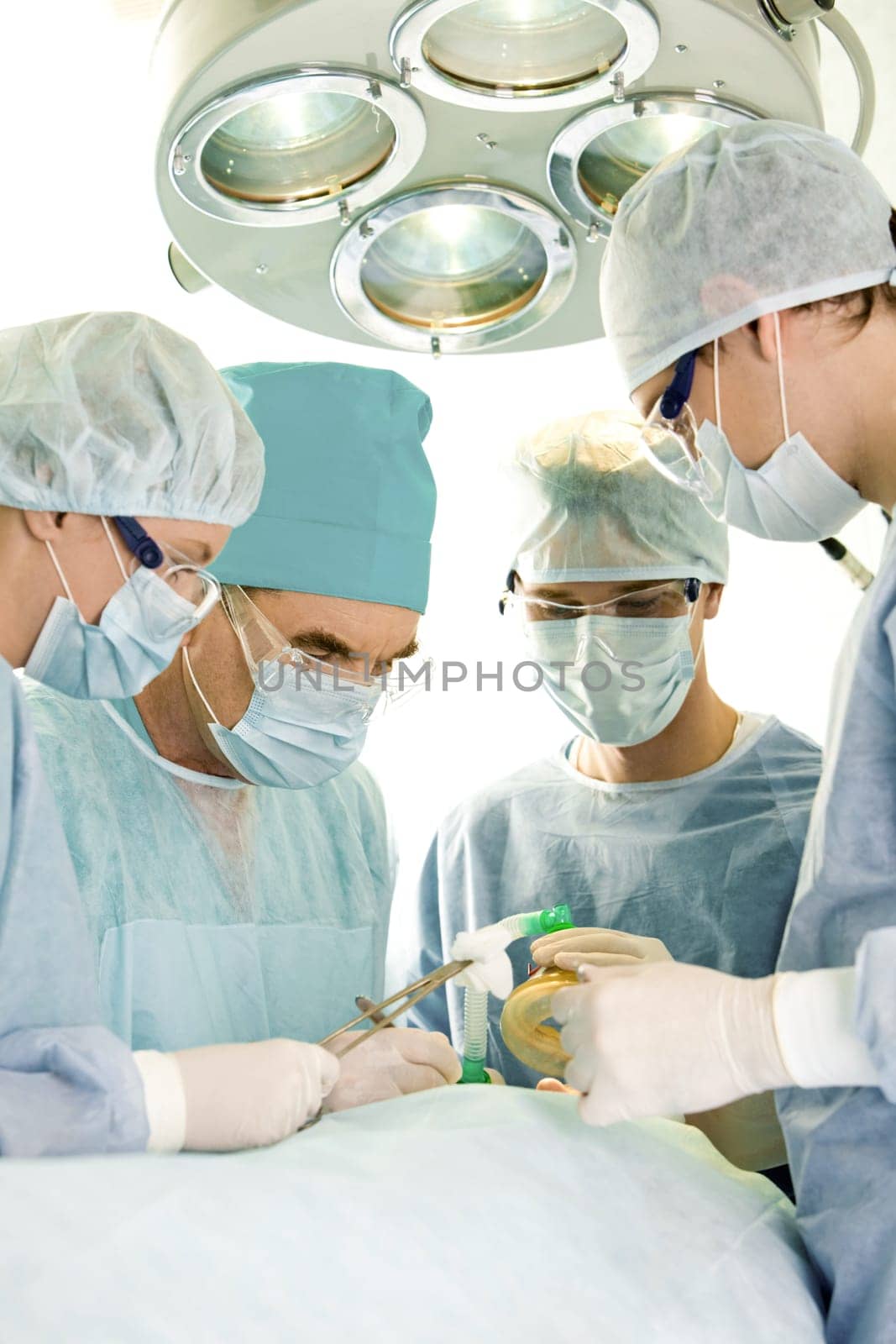 Image of operation: four people in surgical clothes standing near patient