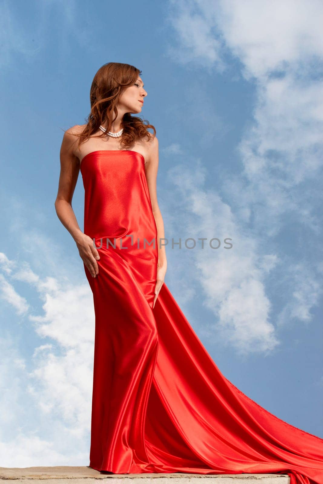 Photo of graceful female folded in bright red silk shawl with cloudy sky at background