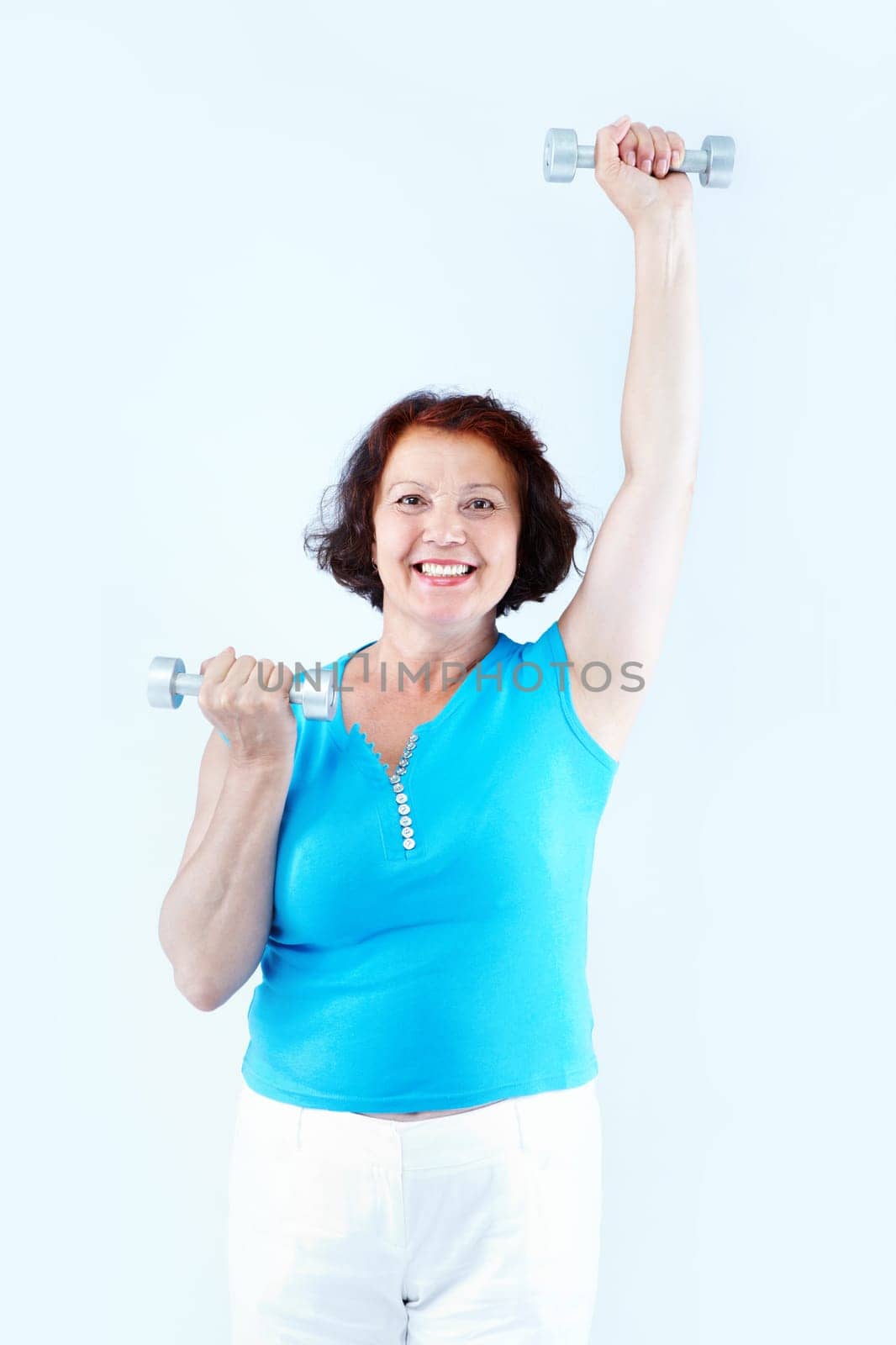 Portrait of healthy middle-aged female with dumbbells raising one arm