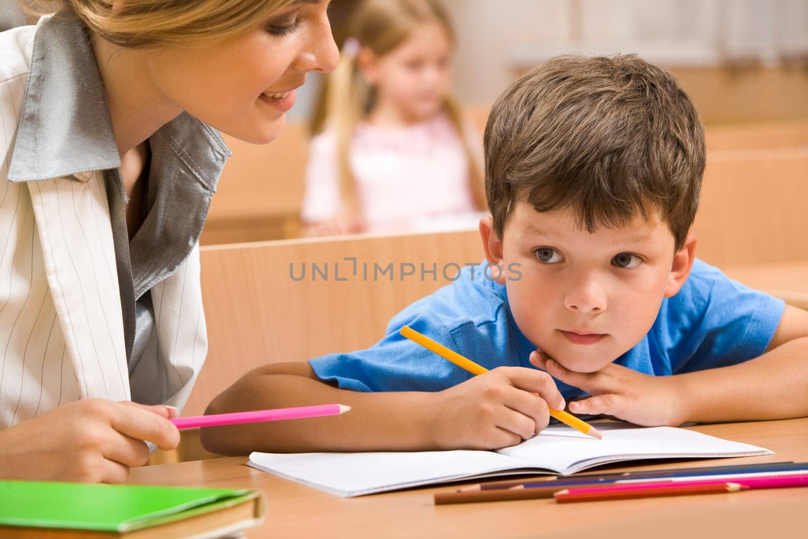 Photo of teacher and schoolboy sitting together at the desk and interacting during lesson