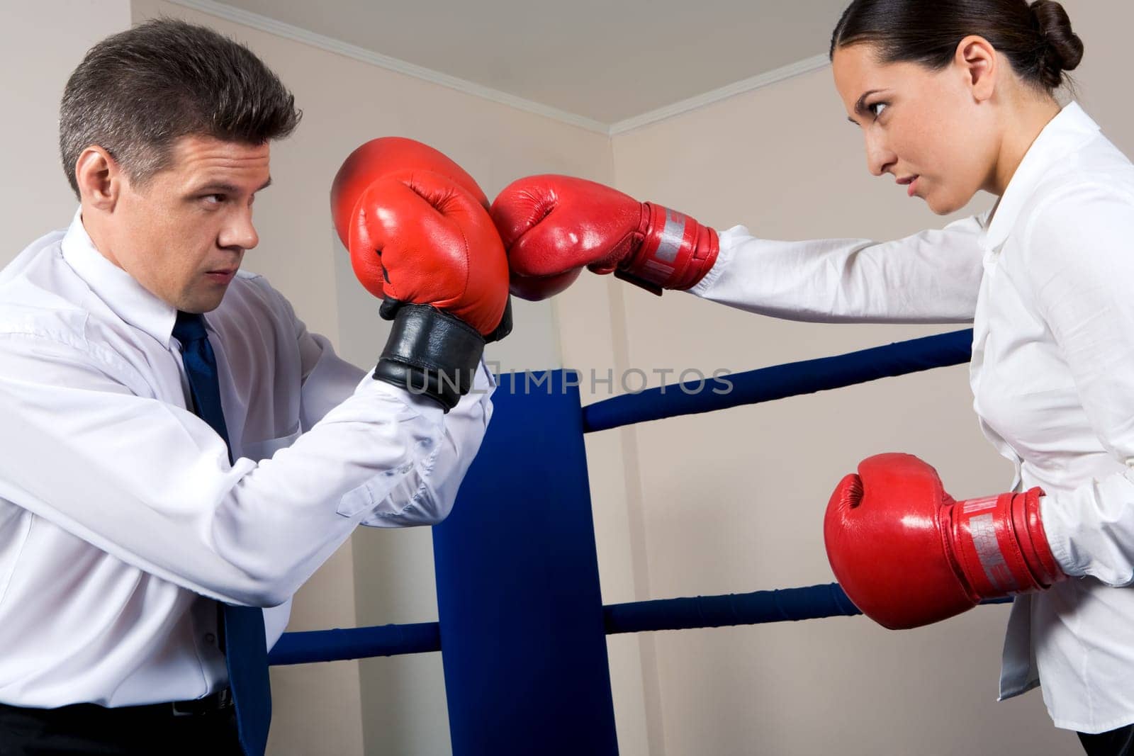 Portrait of aggressive businessman in boxing gloves fighting with serious female opposite him