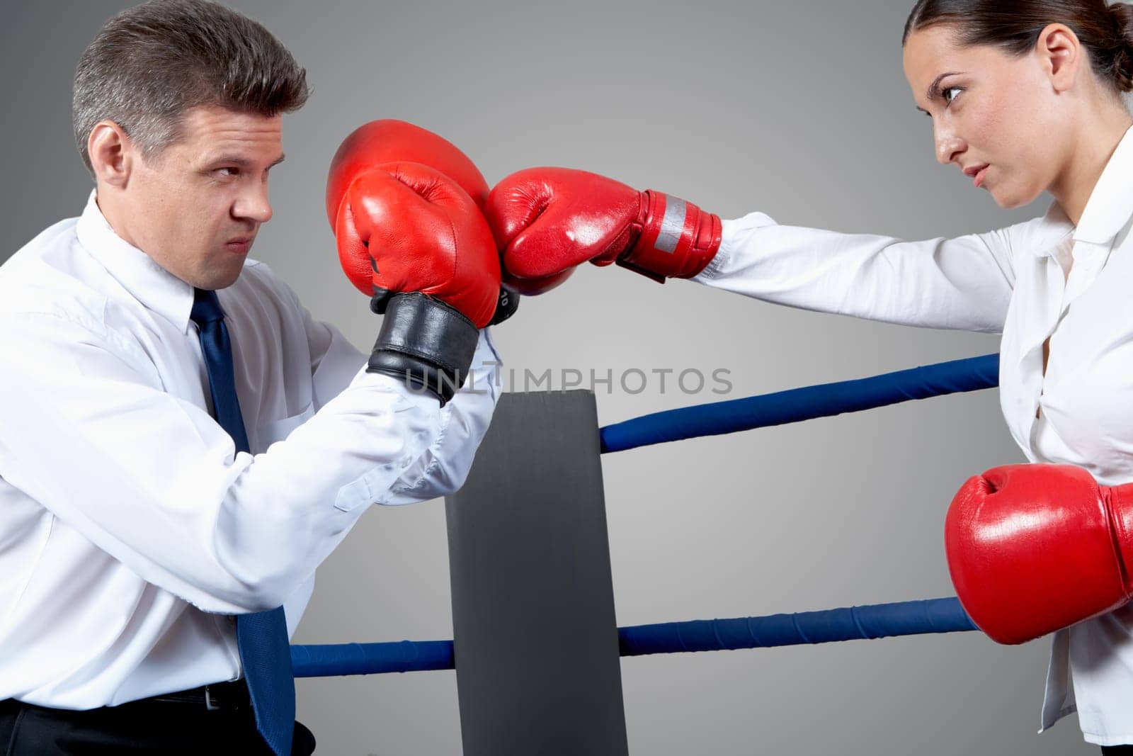 Portrait of aggressive businessman in boxing gloves fighting with serious female opposite him