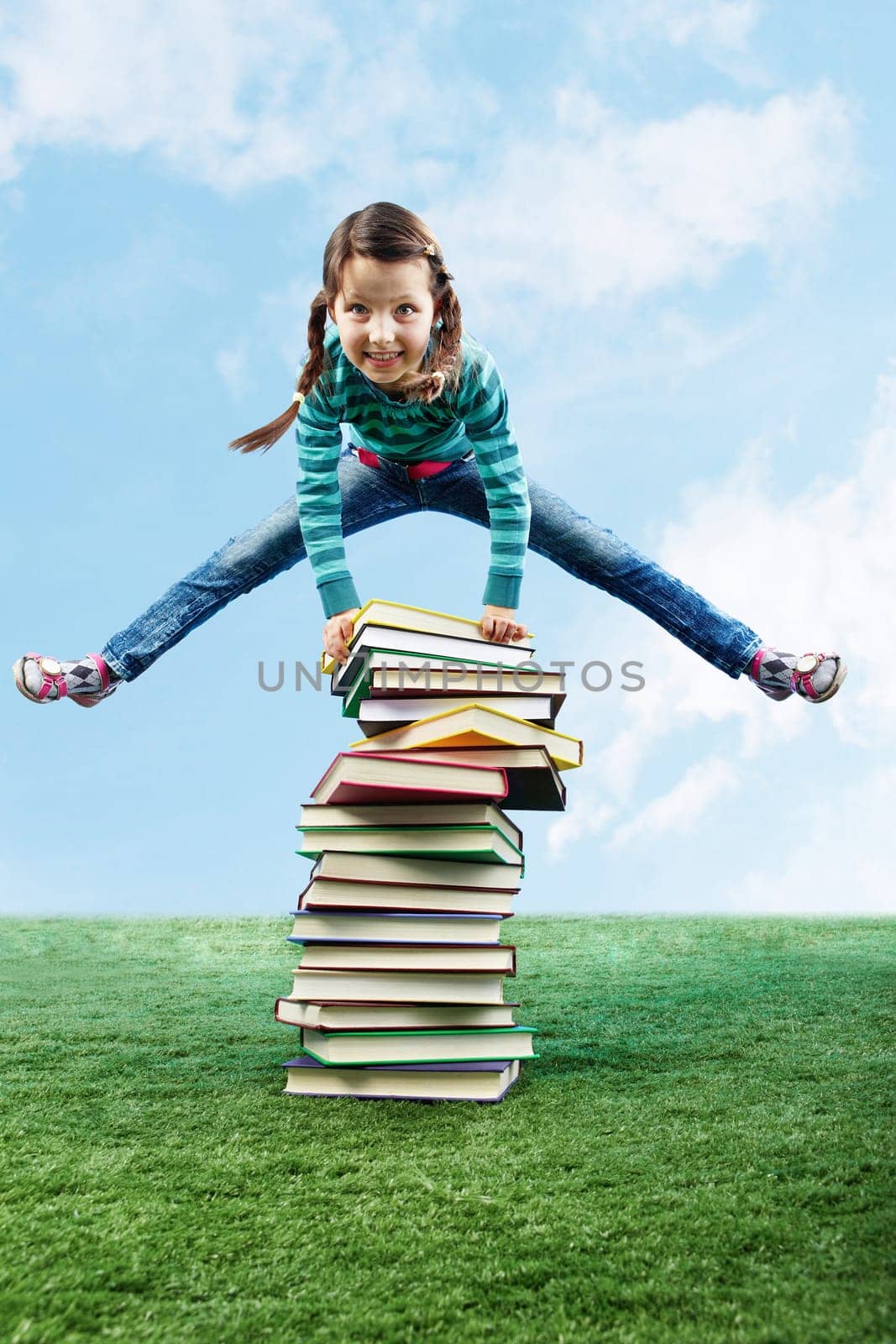 Image of happy girl jumping on the grass through stack of books