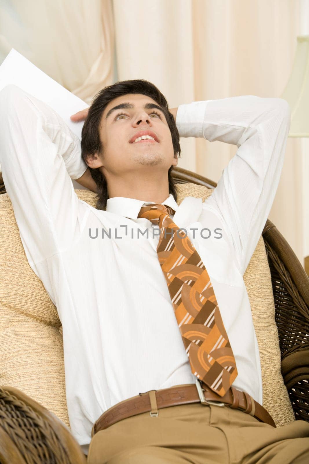 Portrait of positive man relaxing in arm-chair with hands behind head