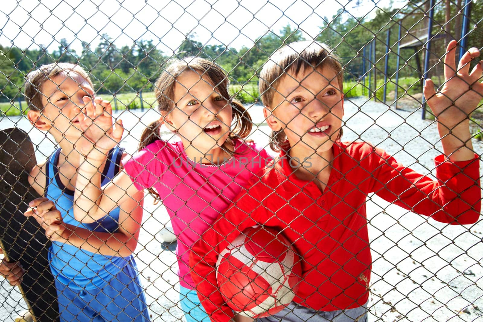 Three children at playground standing behind the netting