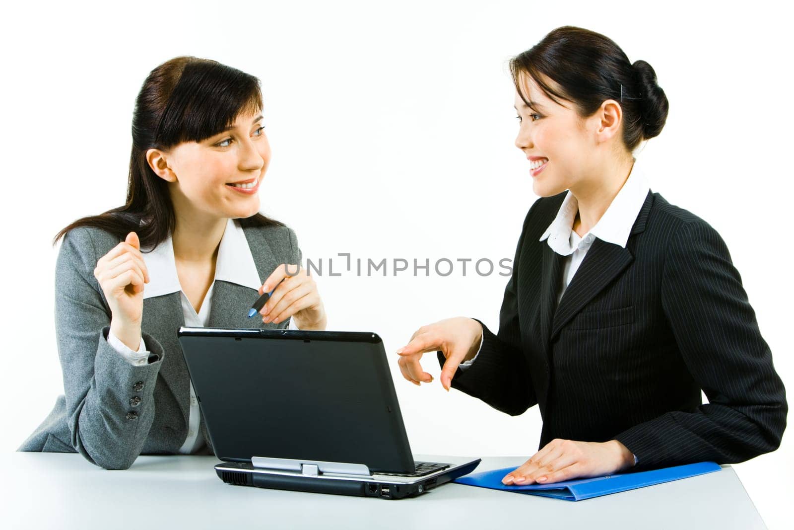 Portrait of two smiling business ladies sitting at laptop pointing at its screen and looking at each other