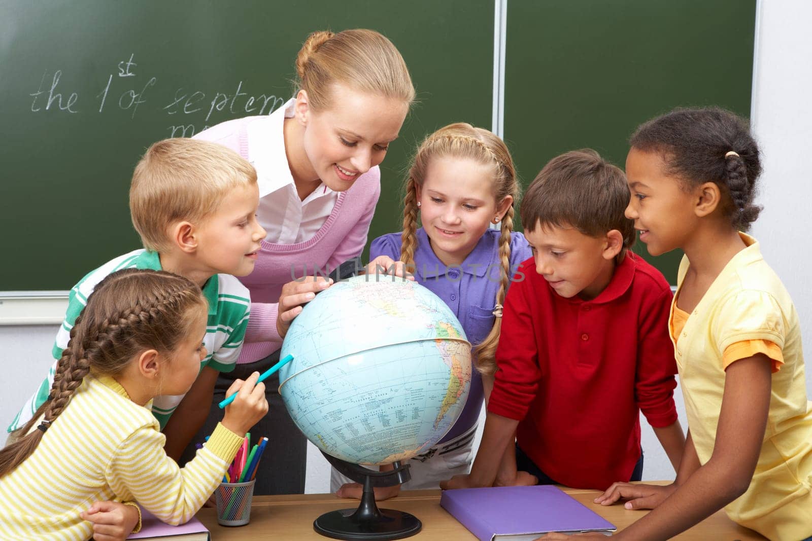 Portrait of pupils looking at globe while listening to teacher during geography lesson