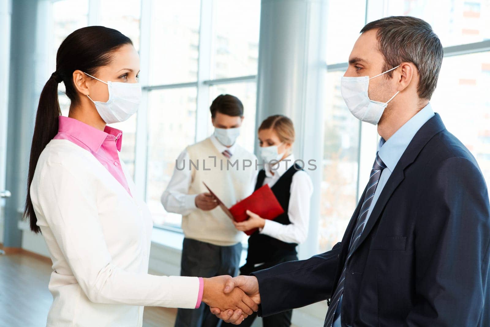 Portrait of successful partners in protective masks handshaking and looking at each other