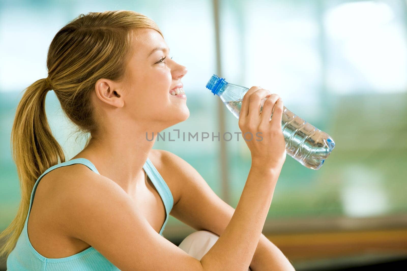 Profile of beautiful woman going to drink some water fron plastic bottle after workout