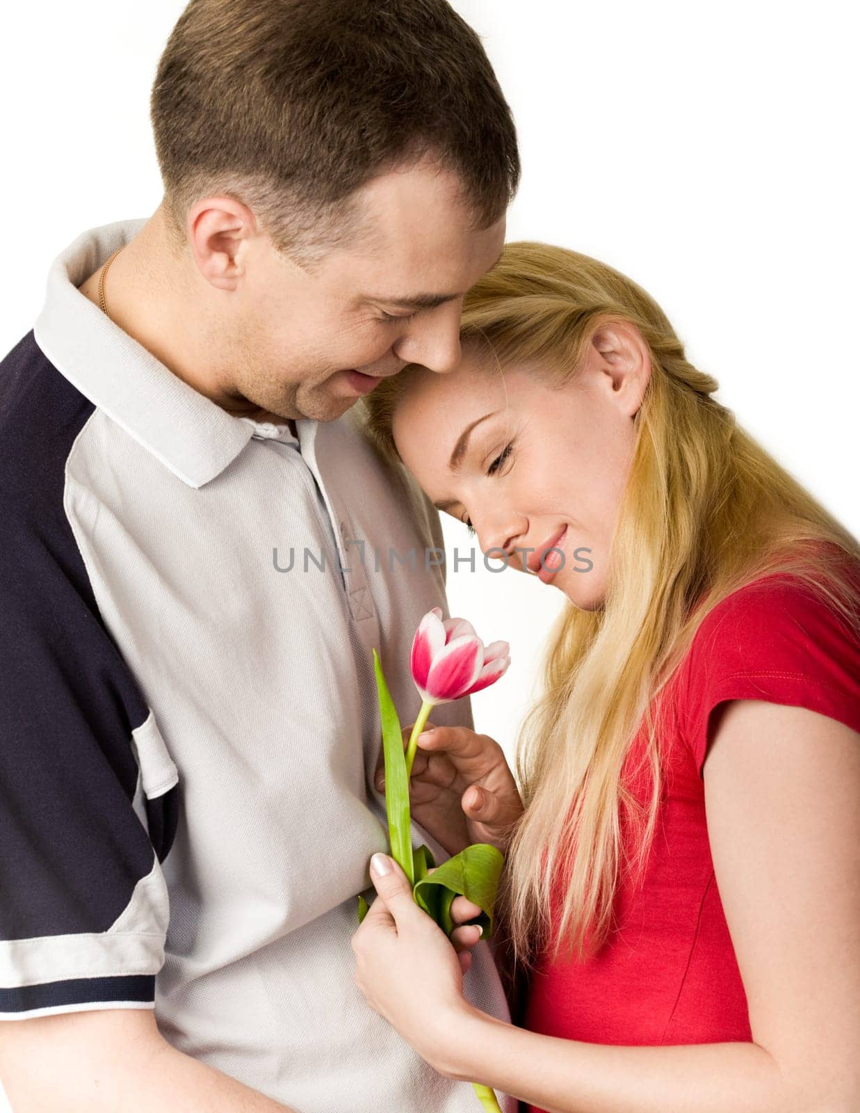 Portrait of pretty woman holding tulip in hand and looking at it with kind man near by