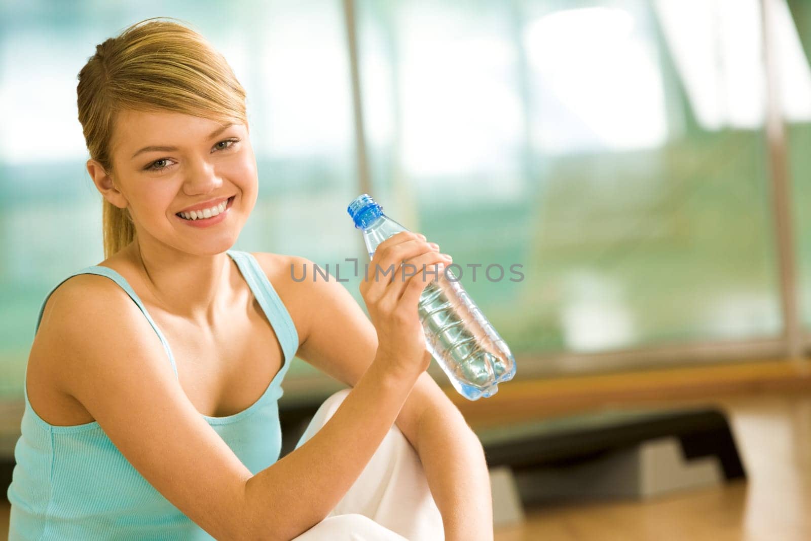 Portrait of lovely girl holding bottle of water in hand and smiling