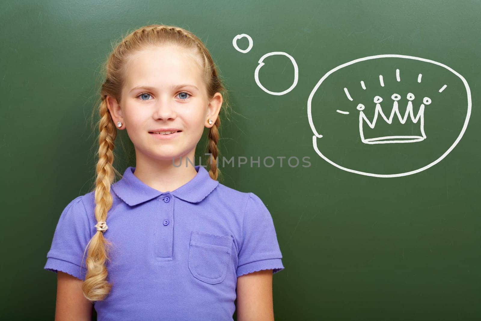 Portrait of smart girl by the blackboard thinking of crown and looking at camera