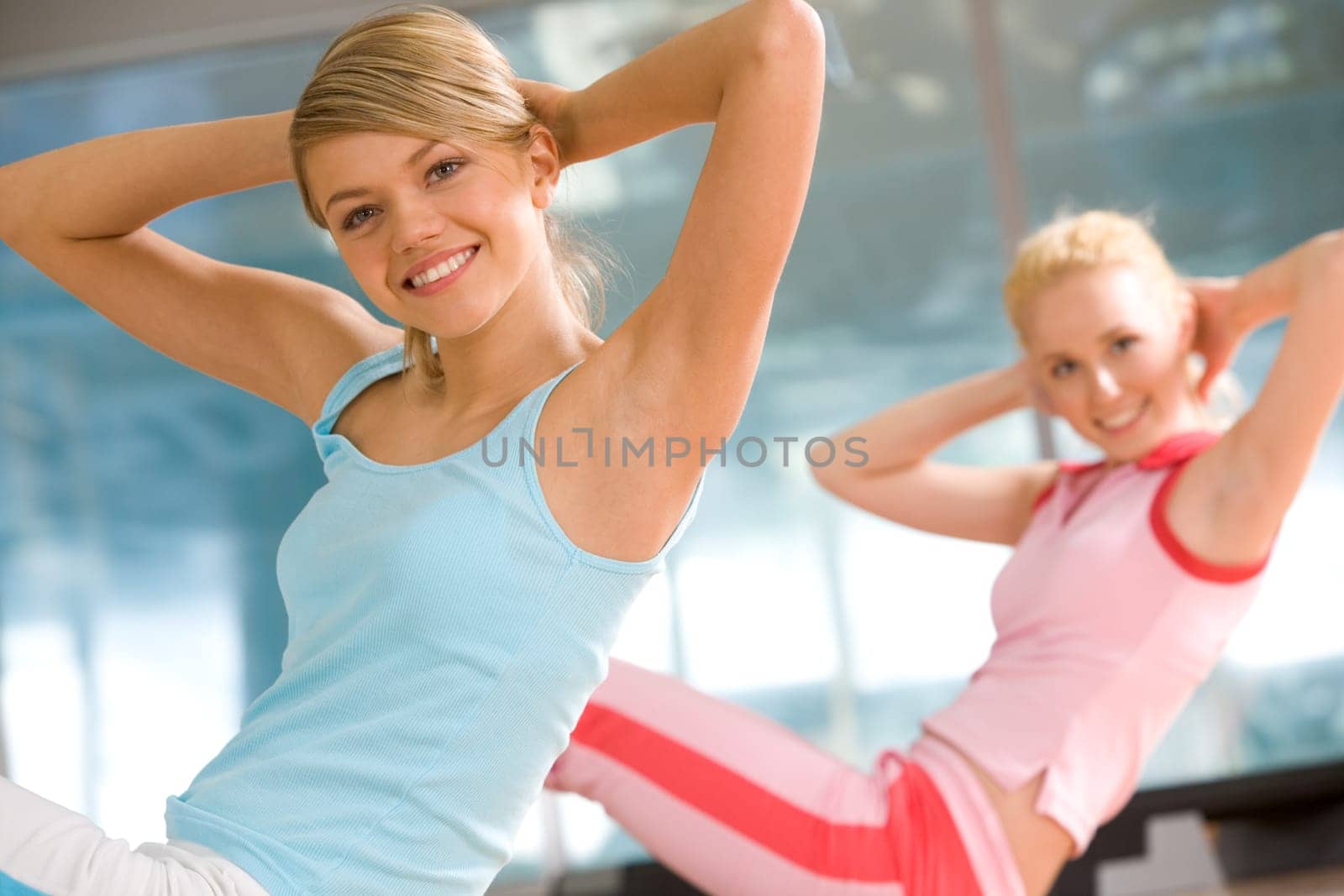 Photo of cheerful girl doing exercise in sport gym with another woman at background