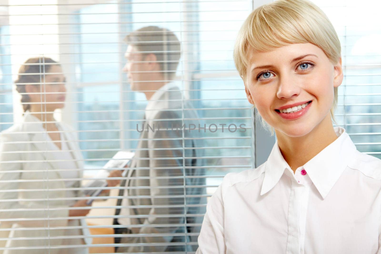 Female leader looking at camera with two partners interacting in office behind