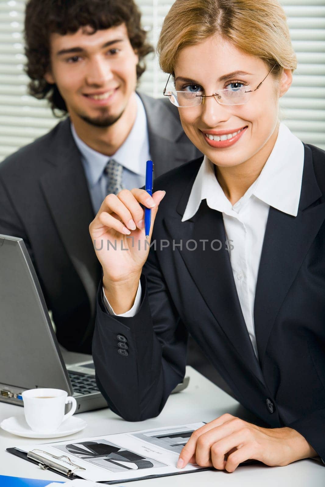 Successful young business woman is holding blue pen and sitting at the table