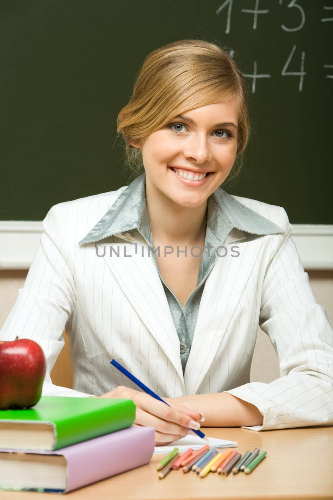 Portrait of young teacher checking copybook with books near by and looking at camera with smile