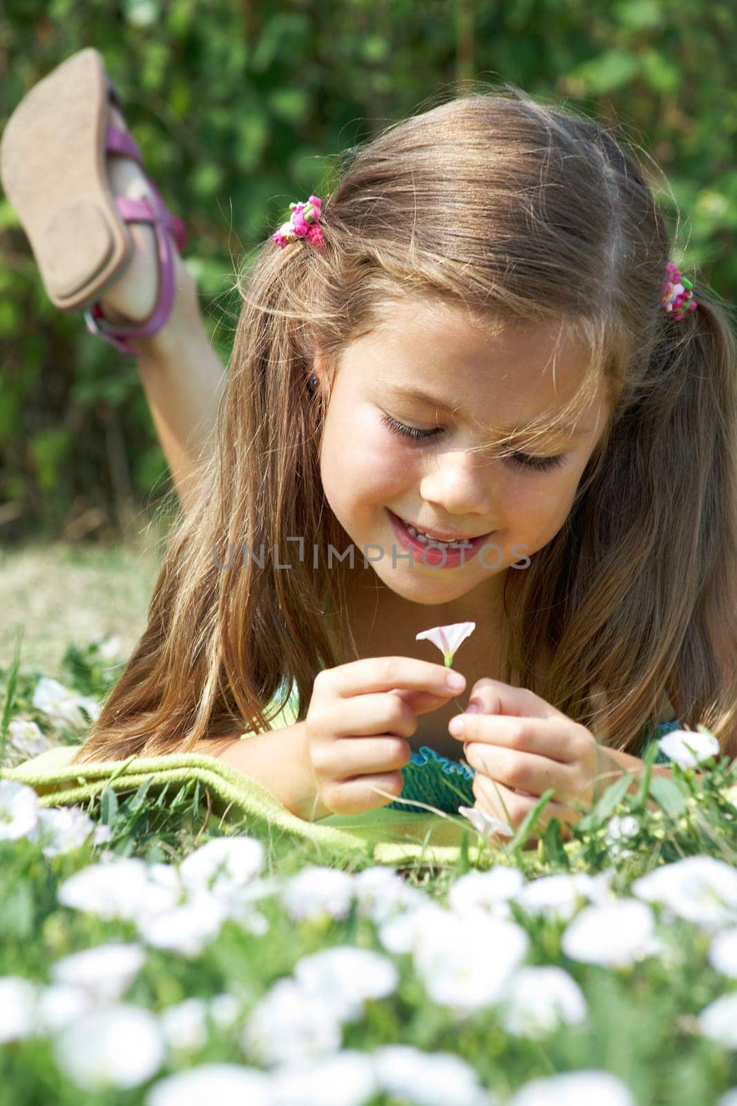 Close-up of girl lying on green grass and enjoying nice smell of tiny flower