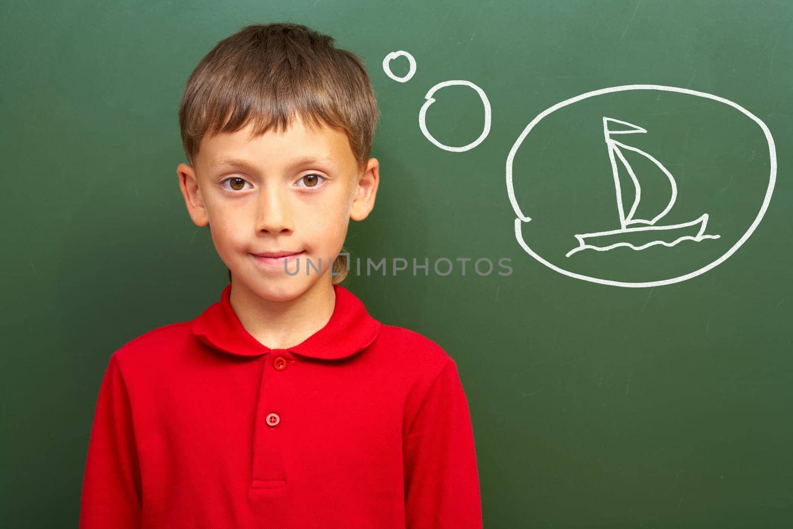 Portrait of smart lad by the blackboard thinking of sail and looking at camera