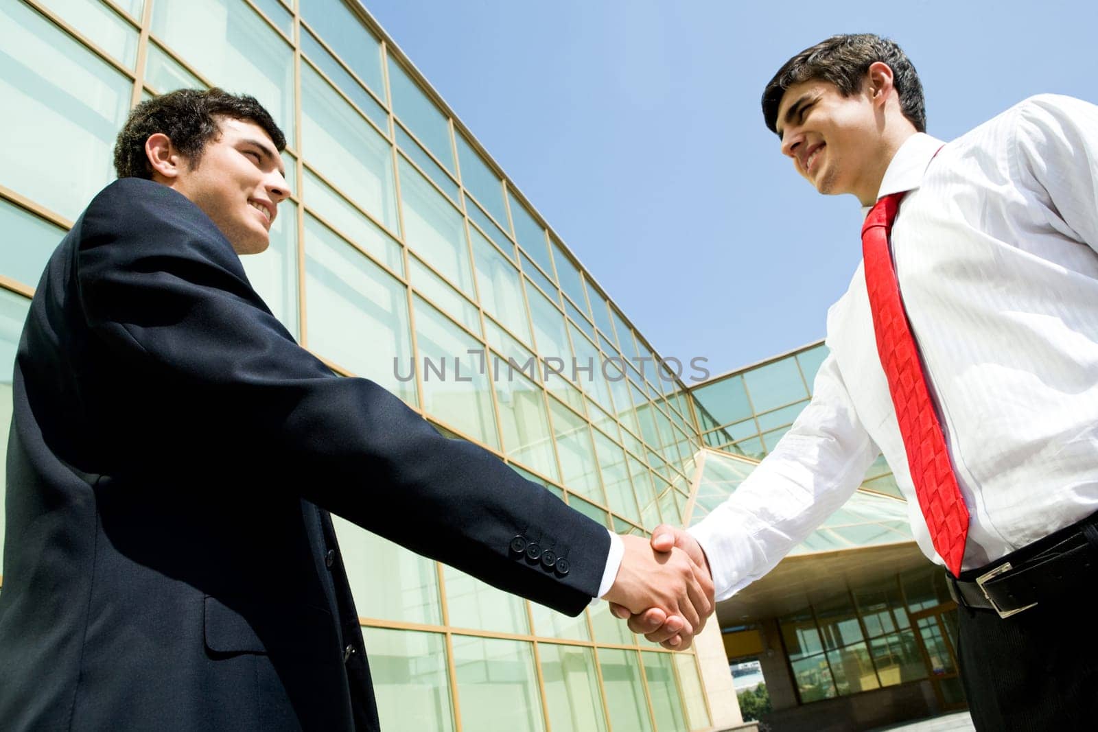 Photo of happy co-workers handshaking outdoors at background of modern building