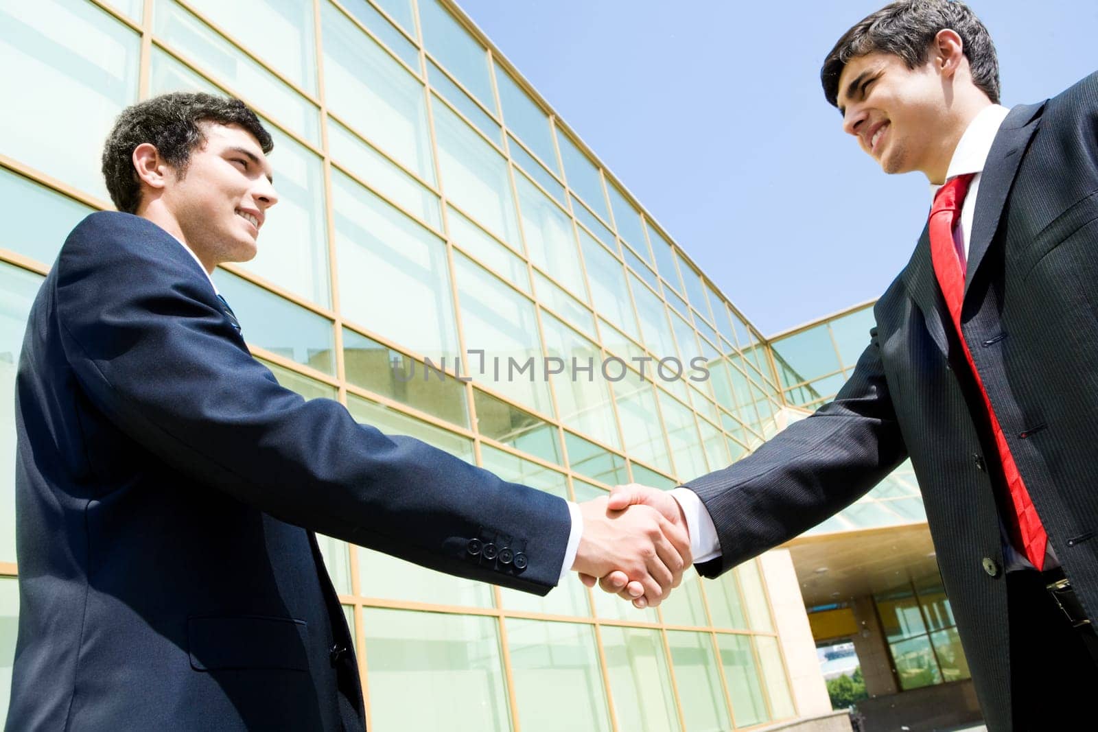 Photo of happy co-workers handshaking outdoors at background of modern building